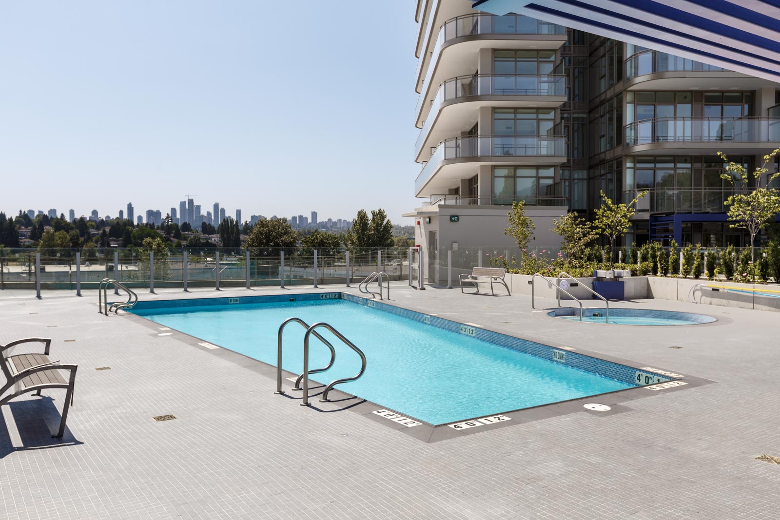 Rooftop swimming pool and hot tub on a modern building with city skyline in the background.
