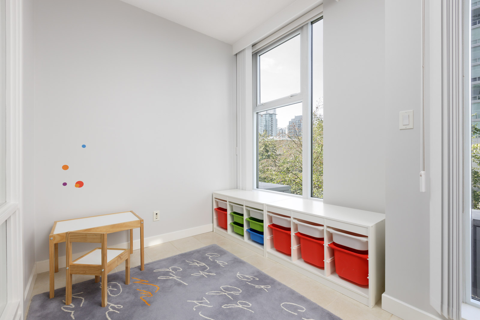 A small playroom with a child's table and chair, colorful storage bins, and large windows letting in natural light.