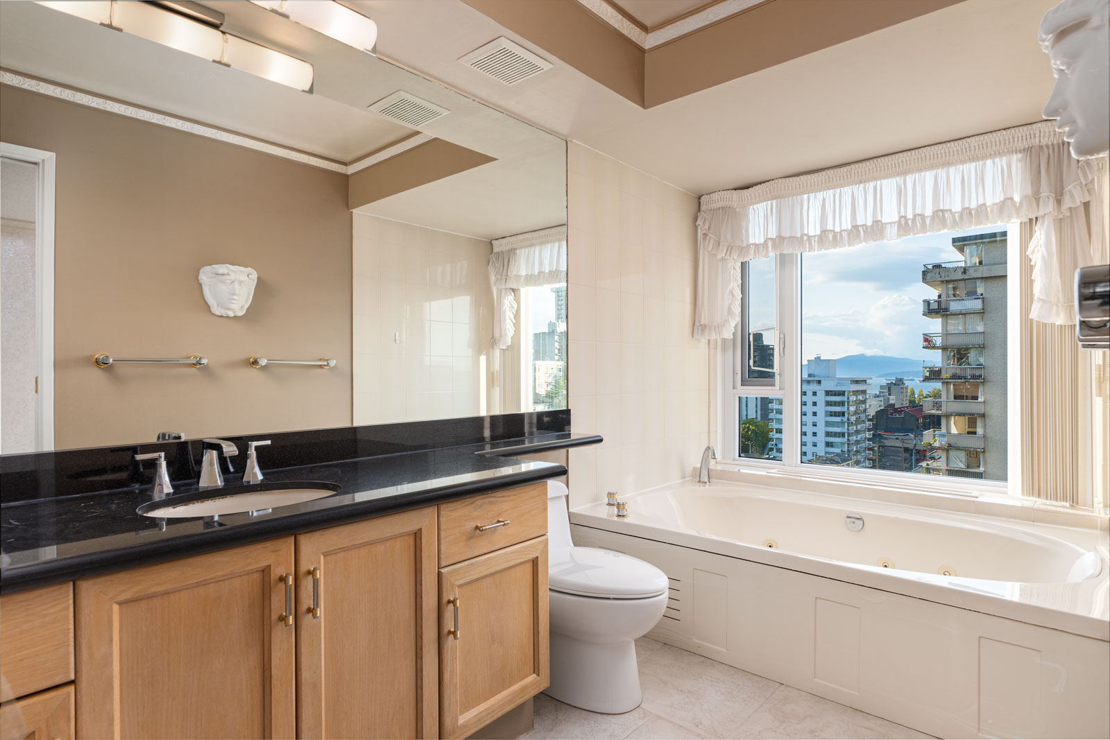 Modern bathroom with a large window view, featuring a wooden vanity, black countertop, bathtub, toilet, and wall-mounted towel racks.