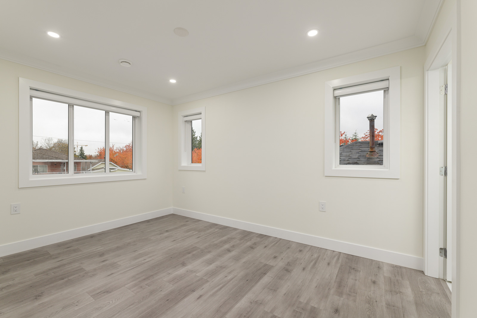 Empty room with light-colored walls, three windows, recessed lighting, and gray wood flooring.