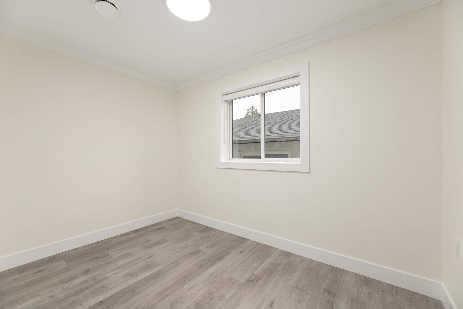 Empty room with light-colored walls, a window with blinds, gray wood flooring, and ceiling light.