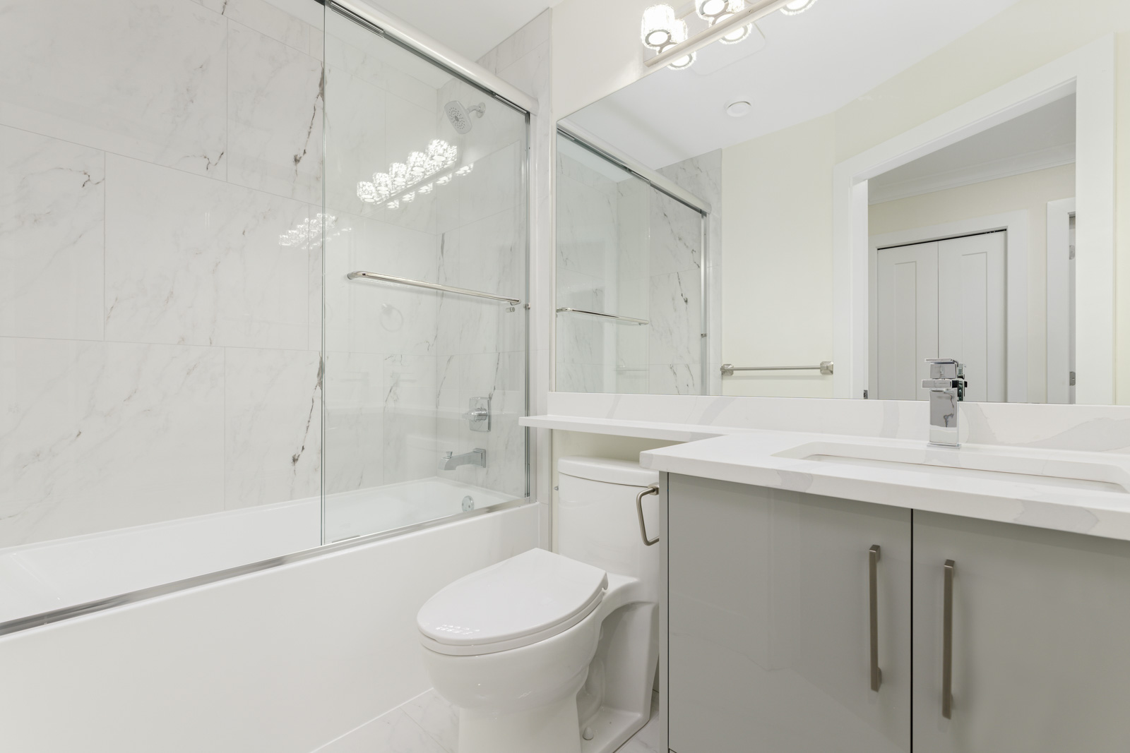 Modern bathroom with a bathtub and shower behind glass doors, a toilet, a white vanity with a sink, and a large mirror above the sink.