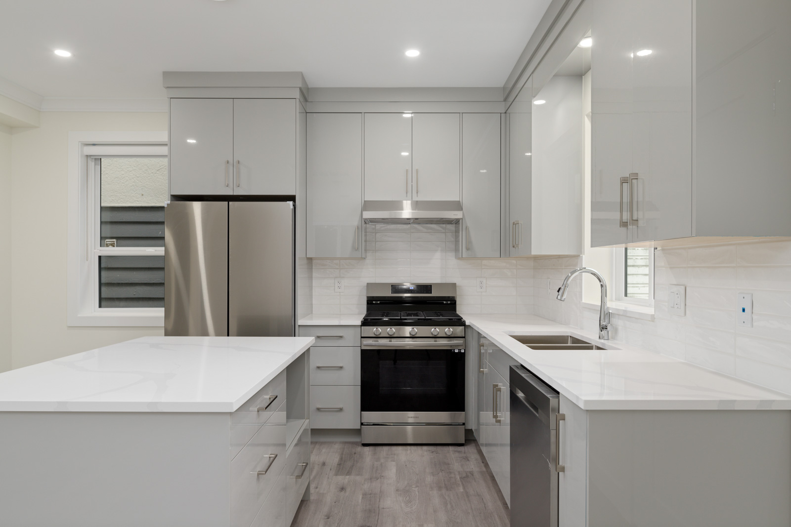 Modern kitchen with glossy gray cabinets, stainless steel appliances, white countertops, an island, and a window above the sink.