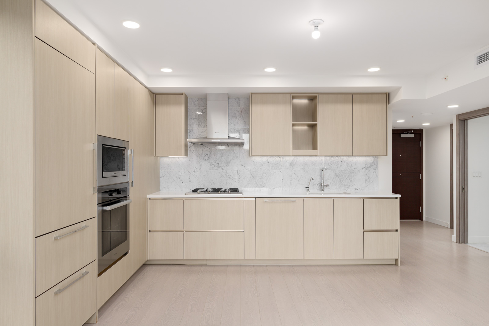Modern kitchen with light wood cabinets, built-in oven, gas stove, marble backsplash, and minimalist design in a bright, open space.