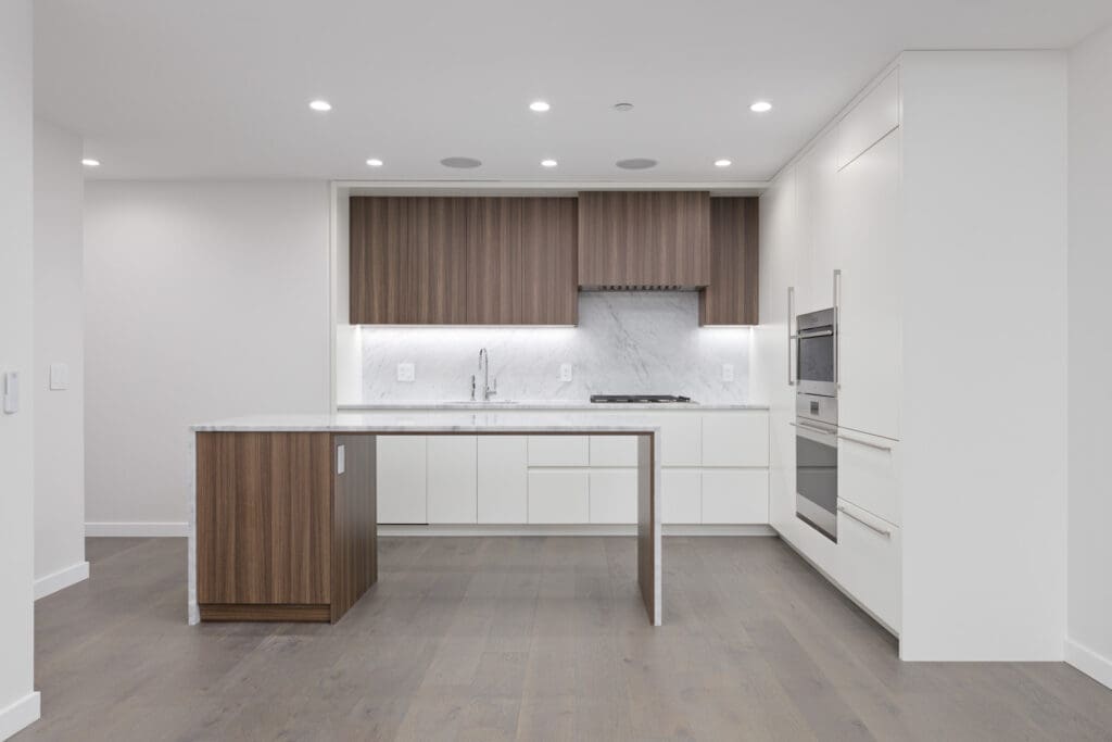 Modern kitchen with wooden island, white cabinetry, marble backsplash, and built-in oven. Pendant lights illuminate the space.
