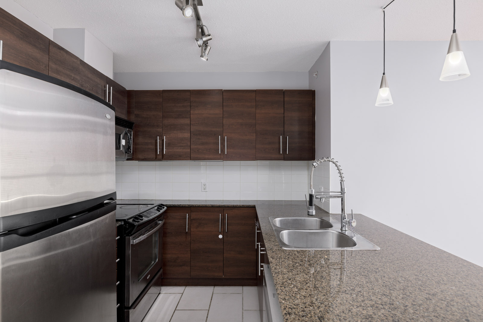 Modern kitchen with dark wood cabinets, stainless steel appliances, double sink, and granite countertop under pendant lights.