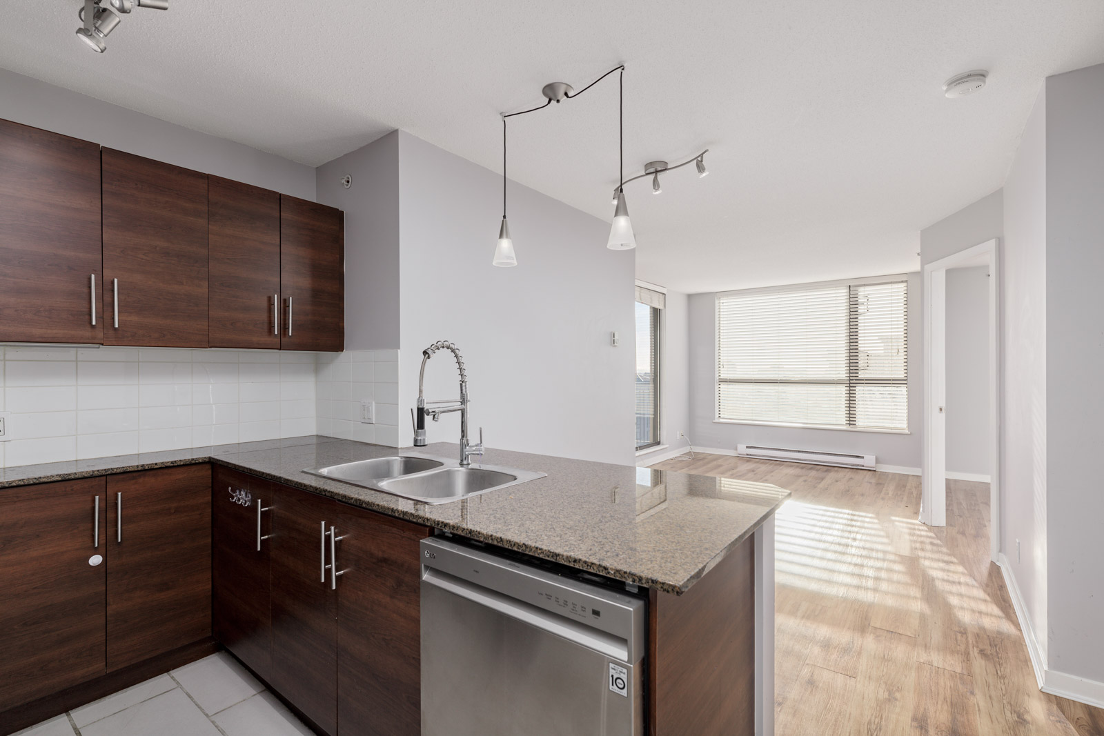 Modern kitchen with wooden cabinets, granite countertops, and stainless steel appliances. Open living area with large windows and laminate flooring.