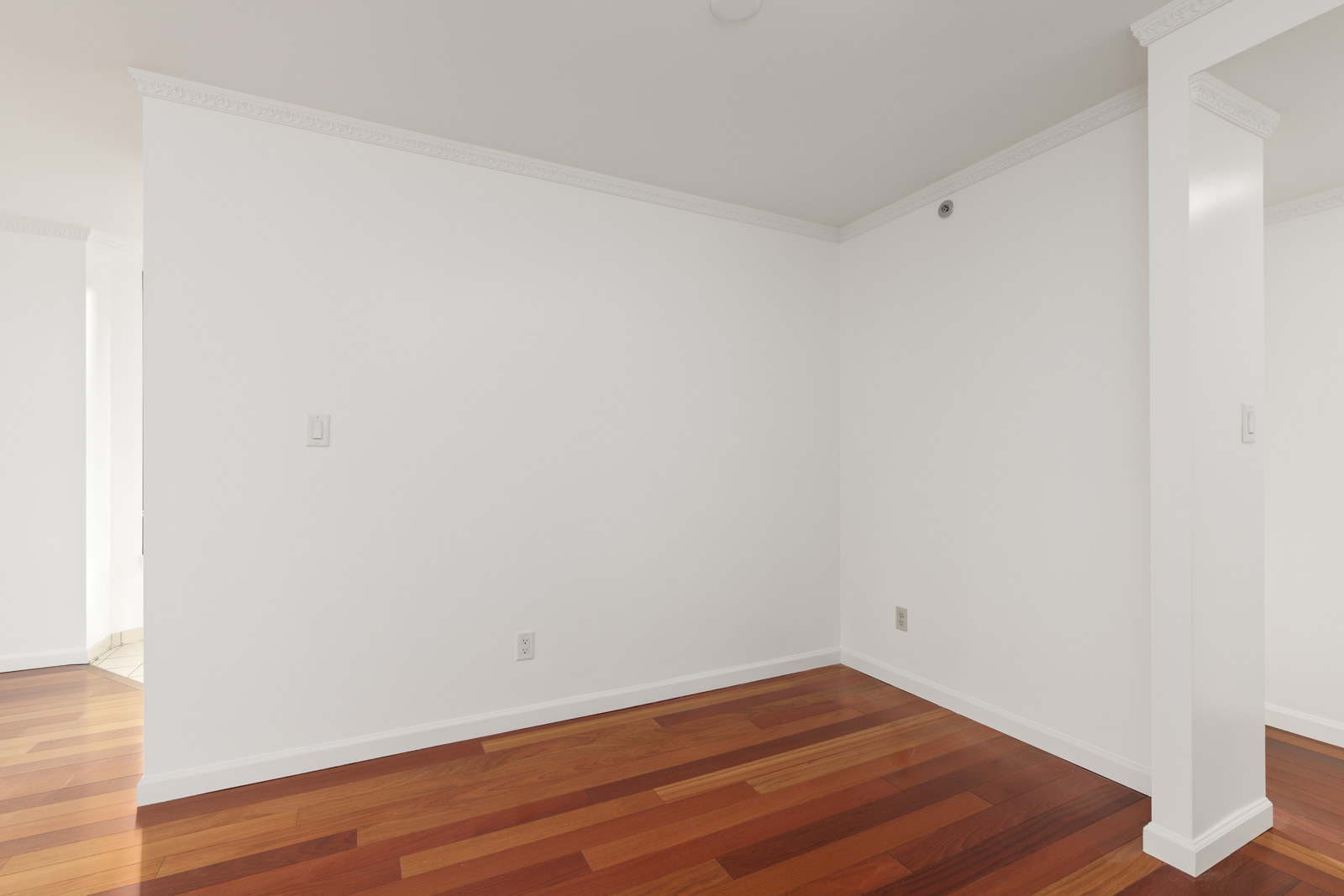 Empty room with white walls, crown molding, hardwood floors, and a partial dividing column; no furniture or decorations are present.
