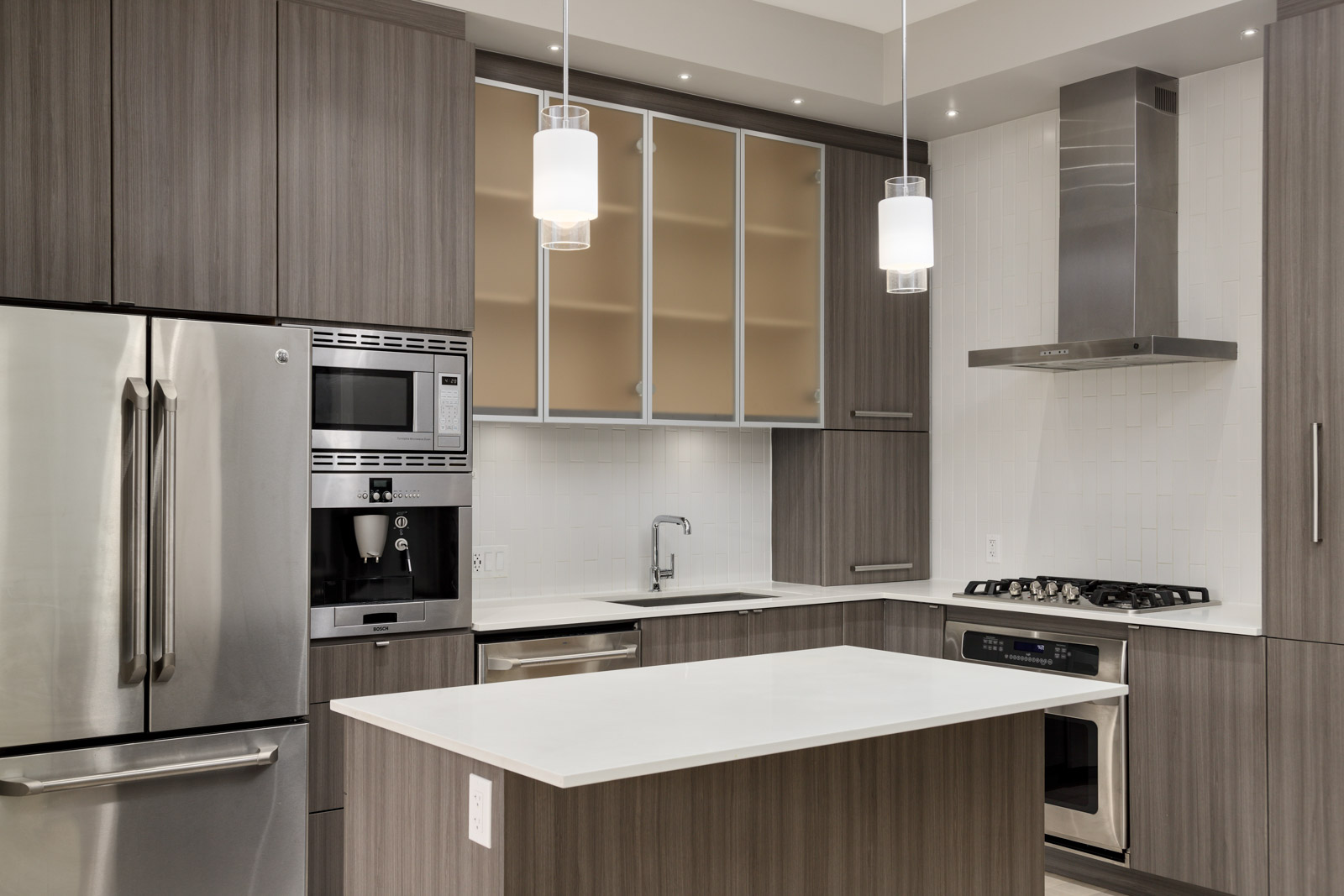 Modern kitchen with gray wooden cabinets, stainless steel appliances, white countertops, an island, and pendant lights above.