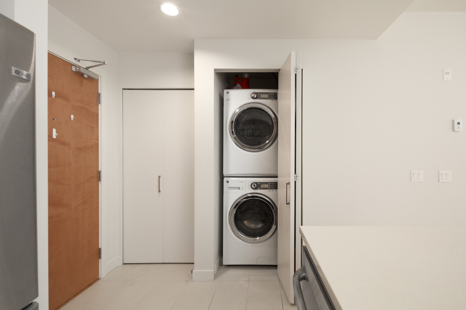Compact laundry area with a stacked washer and dryer in a small alcove next to a closed closet door in a modern interior.
