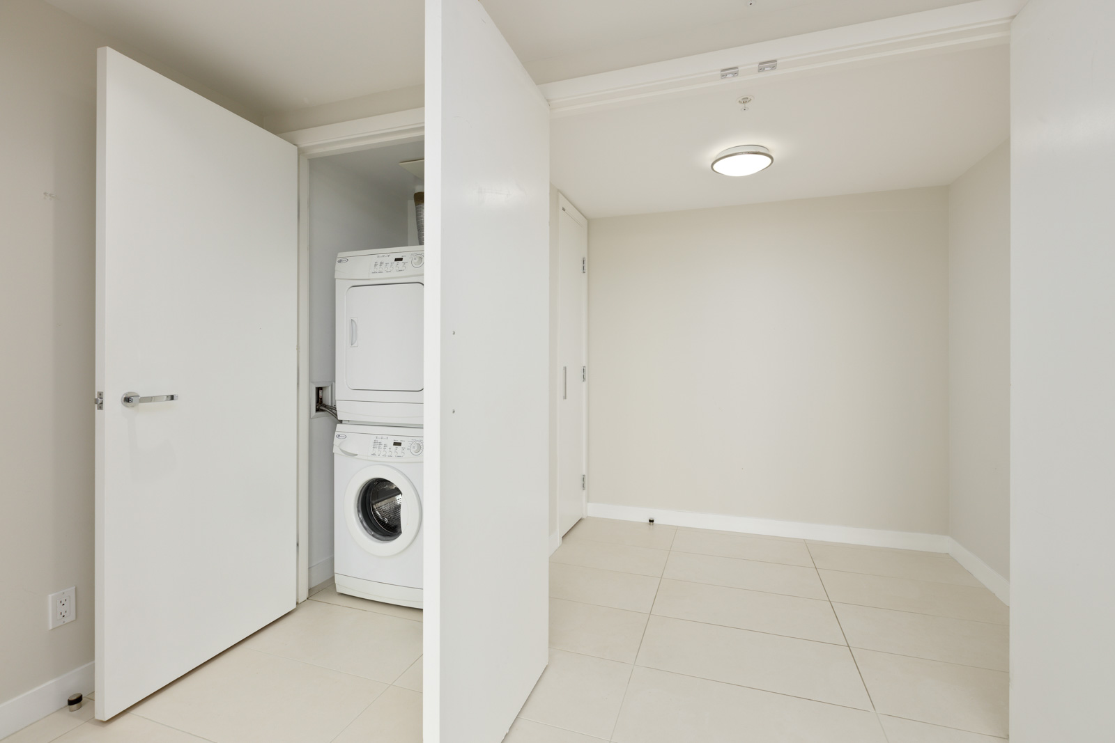 A white stacked washer and dryer set is visible in an open closet within a clean, empty room with tiled floors and neutral-colored walls.