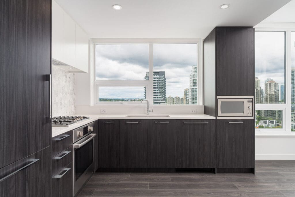 Modern kitchen with dark wood cabinets, stainless steel appliances, a large window with city views, and white countertops.