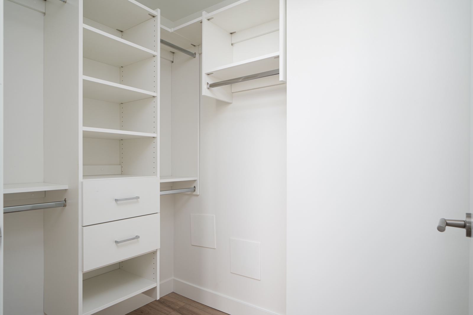 Empty white walk-in closet with open shelving, two drawers, multiple hanging rods, and a wooden floor.