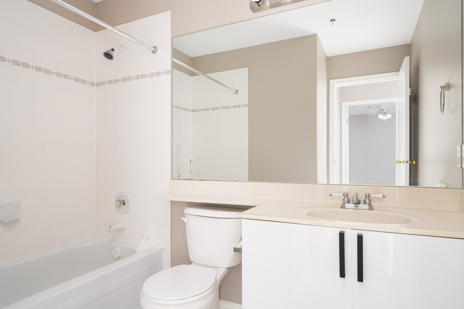 A bathroom featuring a white bathtub, toilet, and sink with a large mirror above the vanity. The walls are painted beige, and there is a small towel ring next to the sink.
