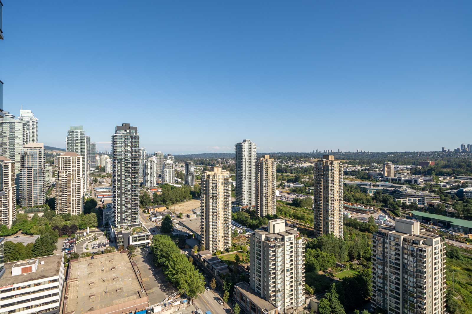 Aerial view of a cityscape featuring numerous tall residential buildings and greenery under a clear blue sky.