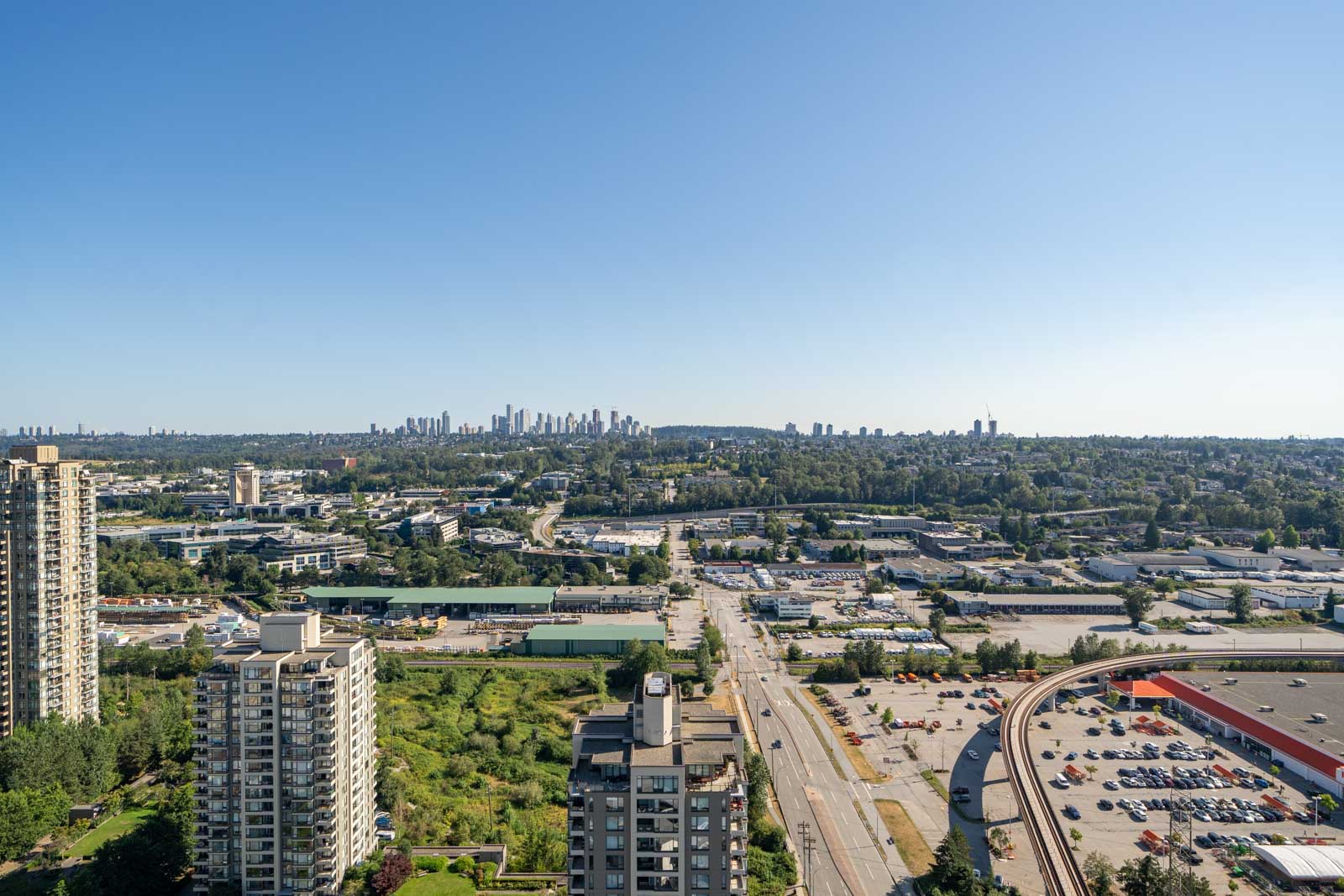 Cityscape view featuring a mix of residential and commercial buildings with a distant downtown skyline beneath a clear blue sky.