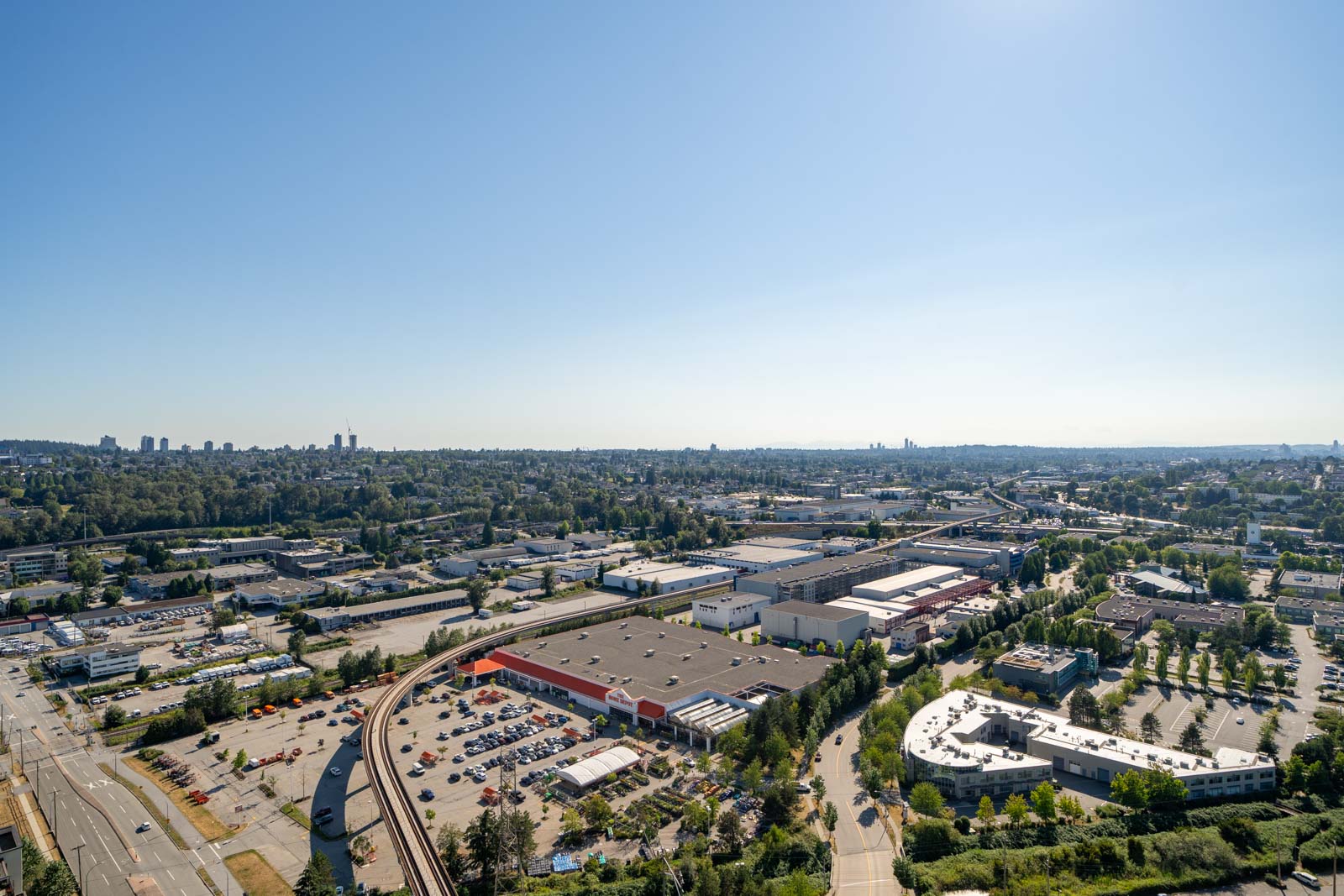 Aerial view of an industrial area with warehouses, roads, and greenery under a clear blue sky.