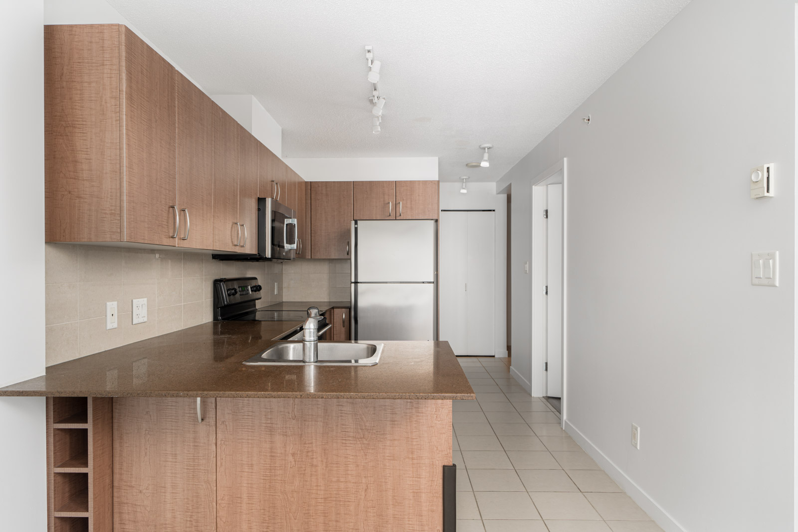 A modern kitchen with wooden cabinets, stainless steel appliances including an oven, microwave, and dishwasher, and a sink on the countertop.