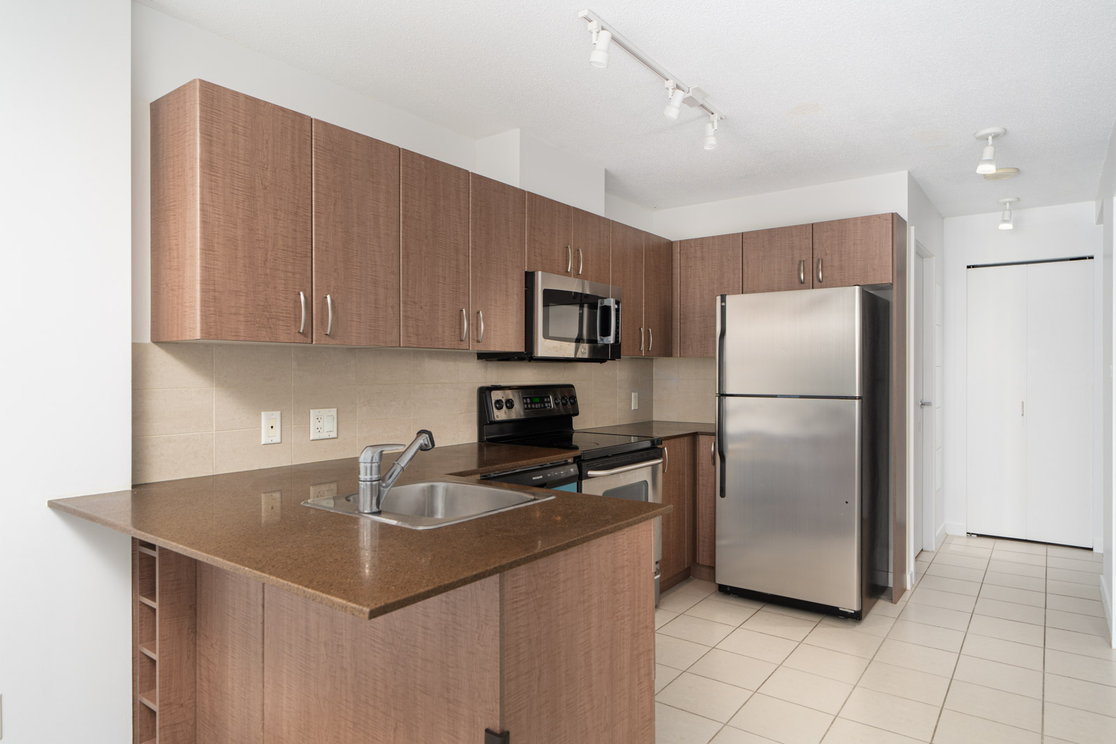 A modern kitchen with wooden cabinets, stainless steel appliances including an oven, microwave, and dishwasher, and a sink on the countertop.