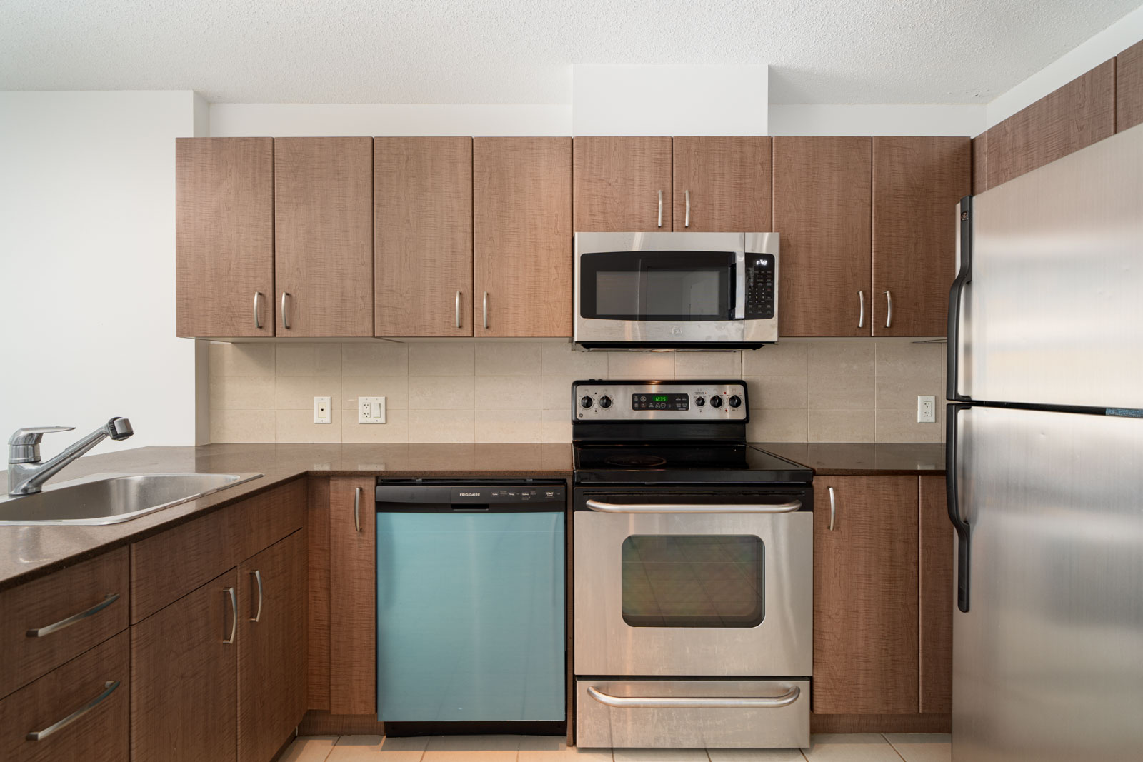 A modern kitchen with wooden cabinets, stainless steel appliances including an oven, microwave, and dishwasher, and a sink on the countertop.