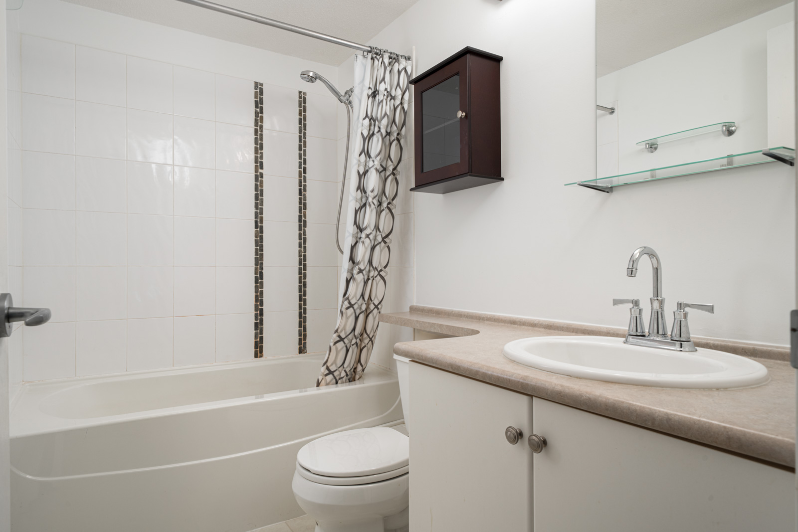 Modern bathroom with chrome fixtures, a countertop sink, a bathtub, a wall-mounted cabinet, and shelves. The space is well-lit and has a neutral color scheme.