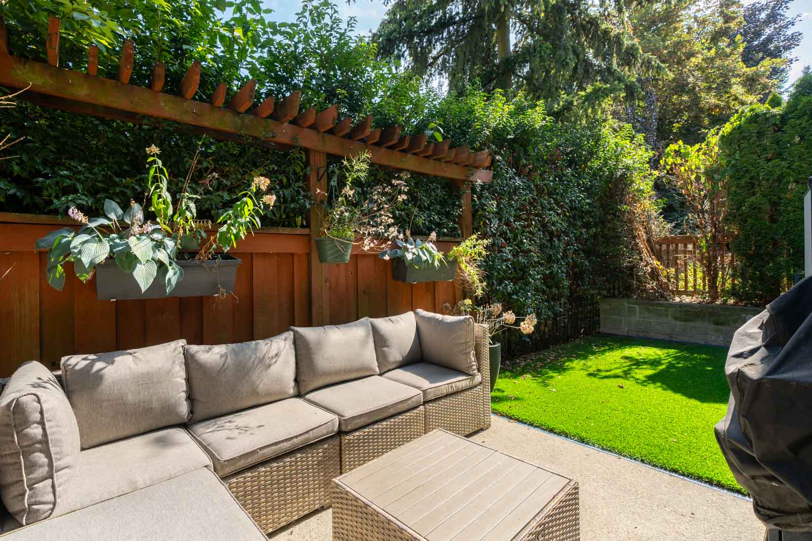 A backyard with patio furniture, a grill, and a green lawn. There is a wooden fence with plants on the left.