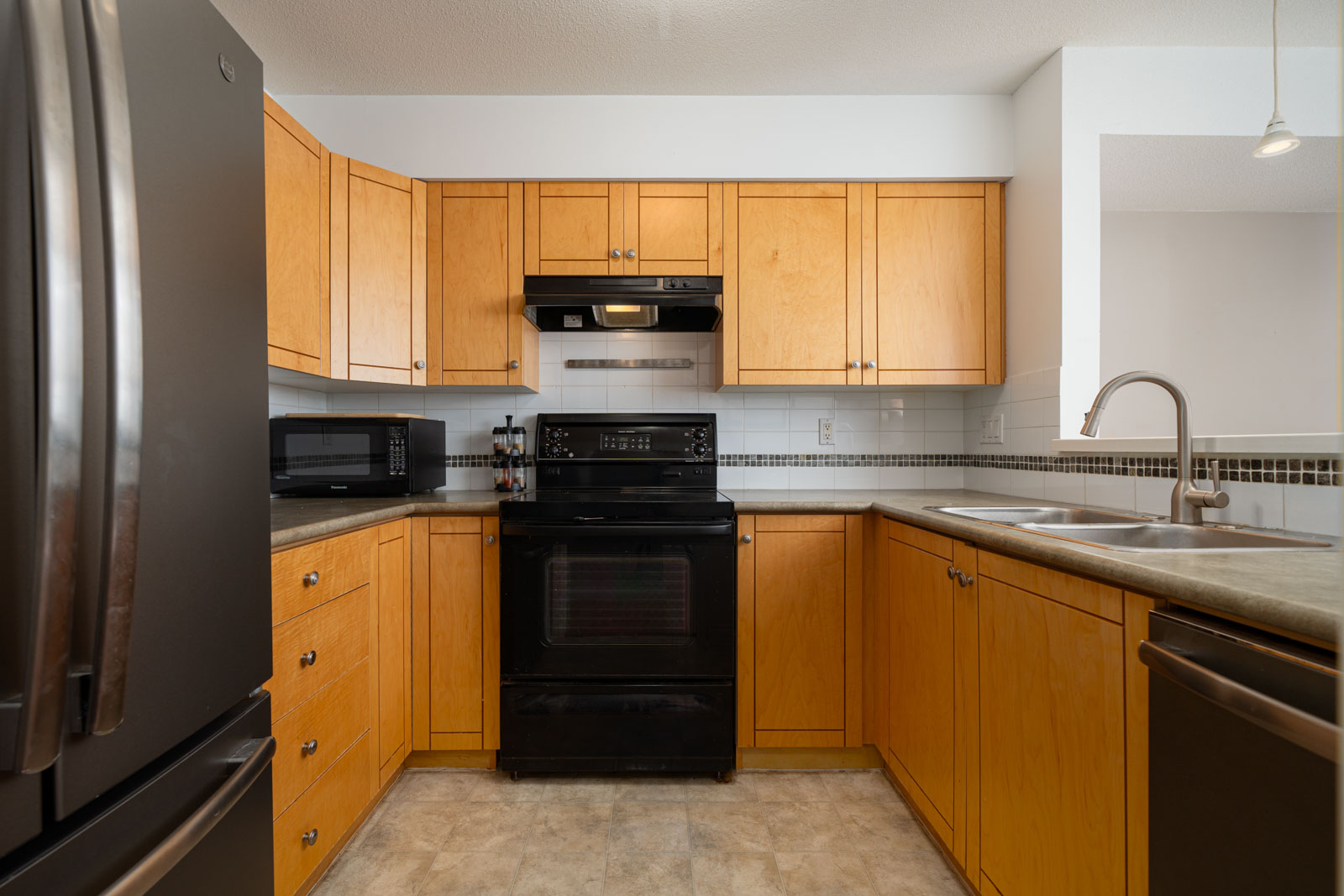 Modern kitchen with wooden cabinets, black appliances including a refrigerator and stove, and a double sink. The countertops are grey and there is a microwave on the left side of the kitchen.