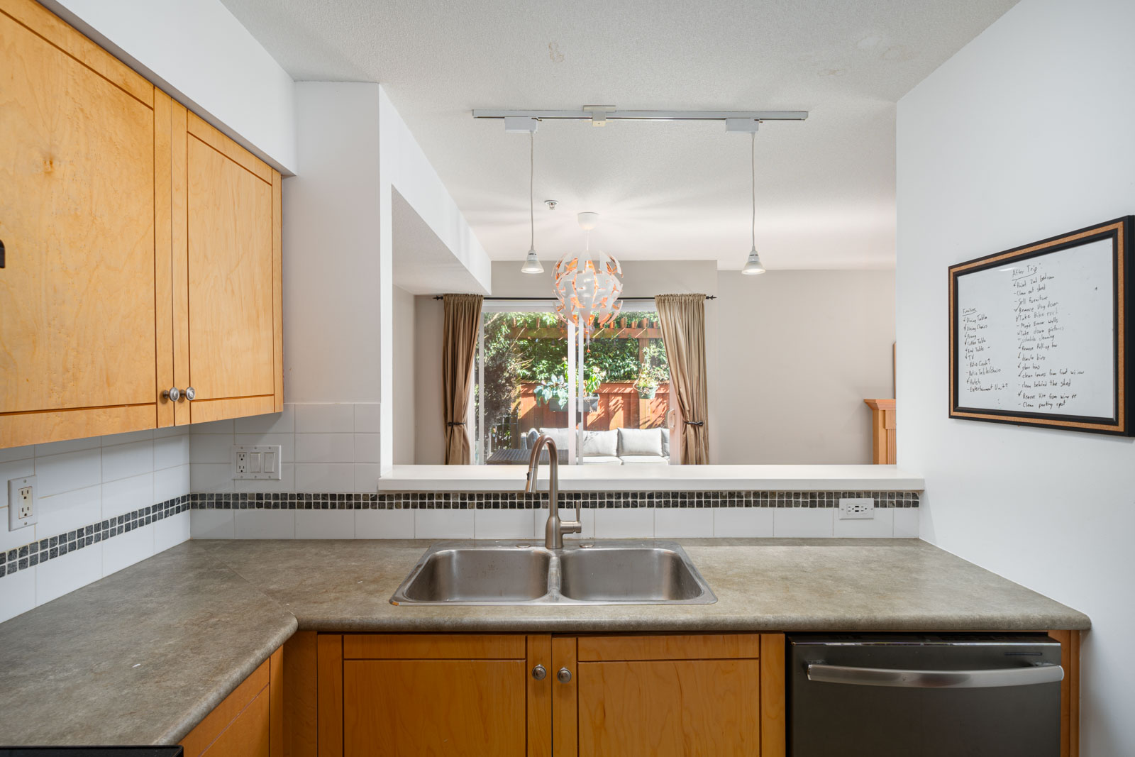 A view from the kitchen featuring a double sink, wooden cabinets, and a laminate countertop. The space opens to a living area with a chandelier and a large window.