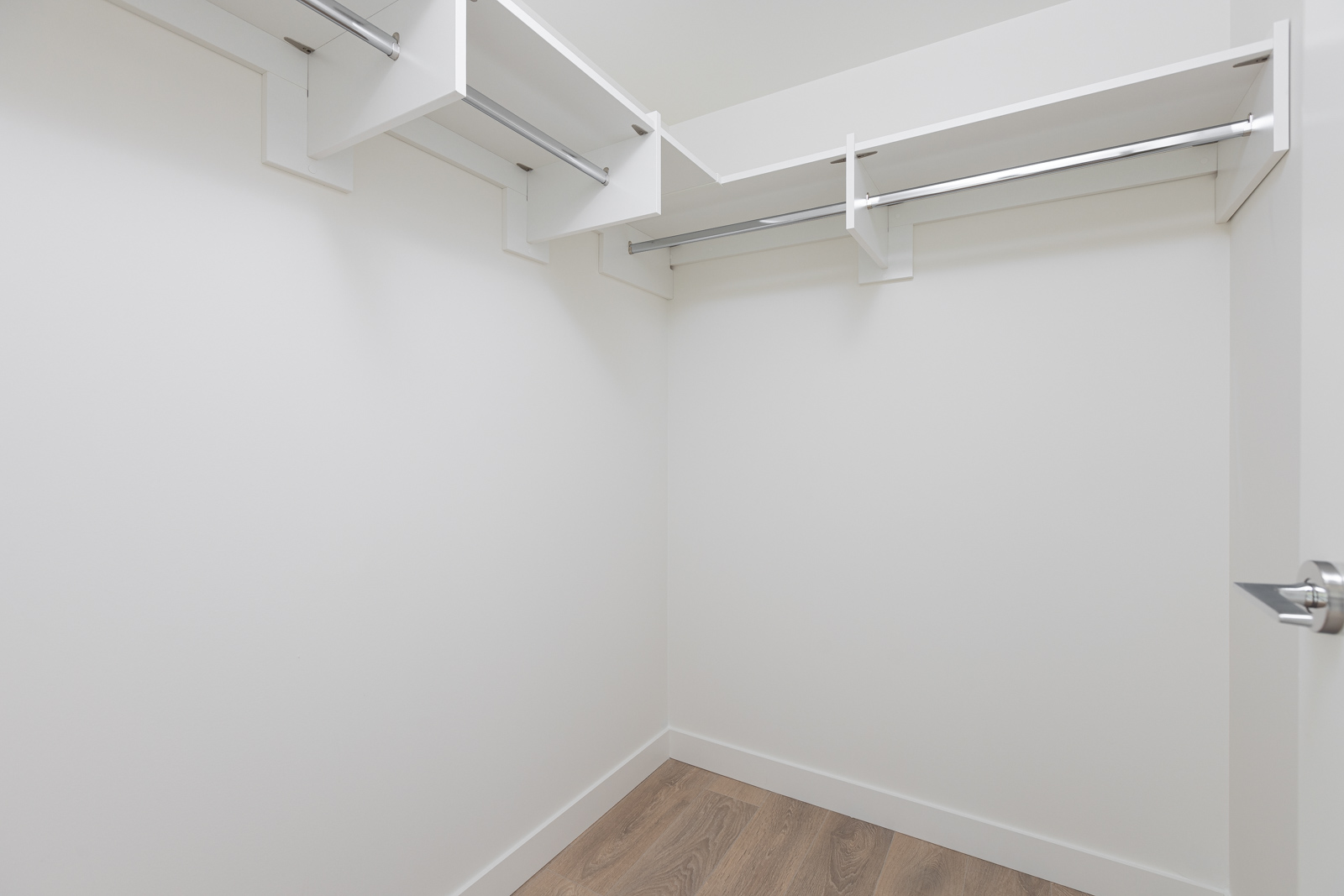 An empty walk-in closet with white walls, wooden flooring, and metal rods and shelves for hanging and storage.