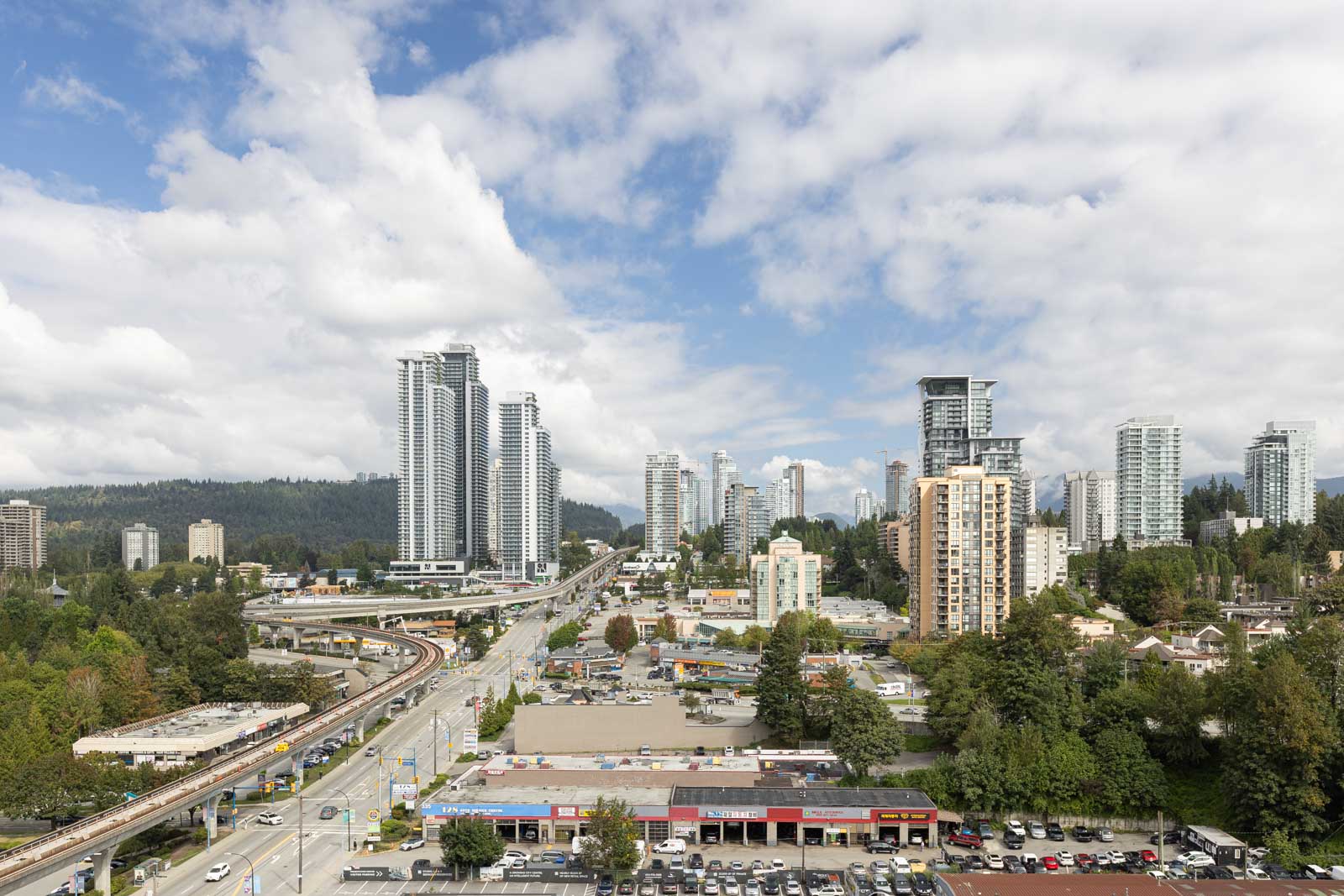 A cityscape featuring high-rise buildings, a major roadway, and scattered trees under a partly cloudy sky.