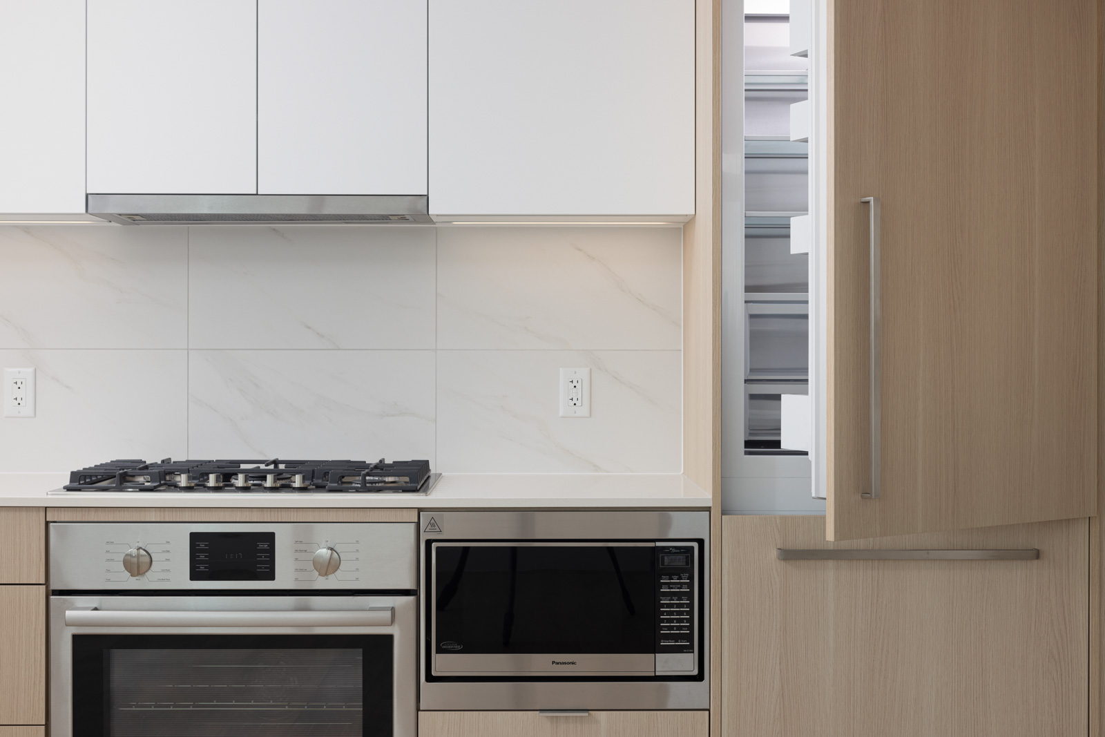 Modern kitchen with a stainless steel gas stove and built-in oven, white cabinets, and a microwave placed under the counter. Light wood panels decorate the right side.