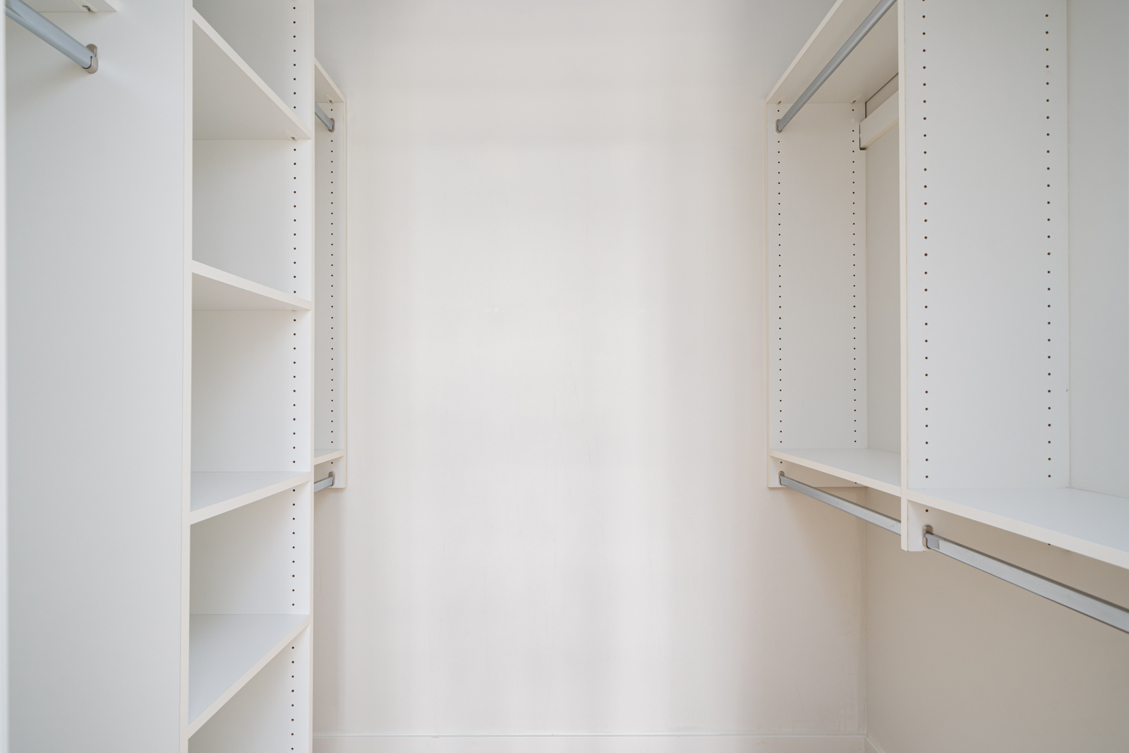 A white walk-in closet with empty shelves and hanging rods on both sides.