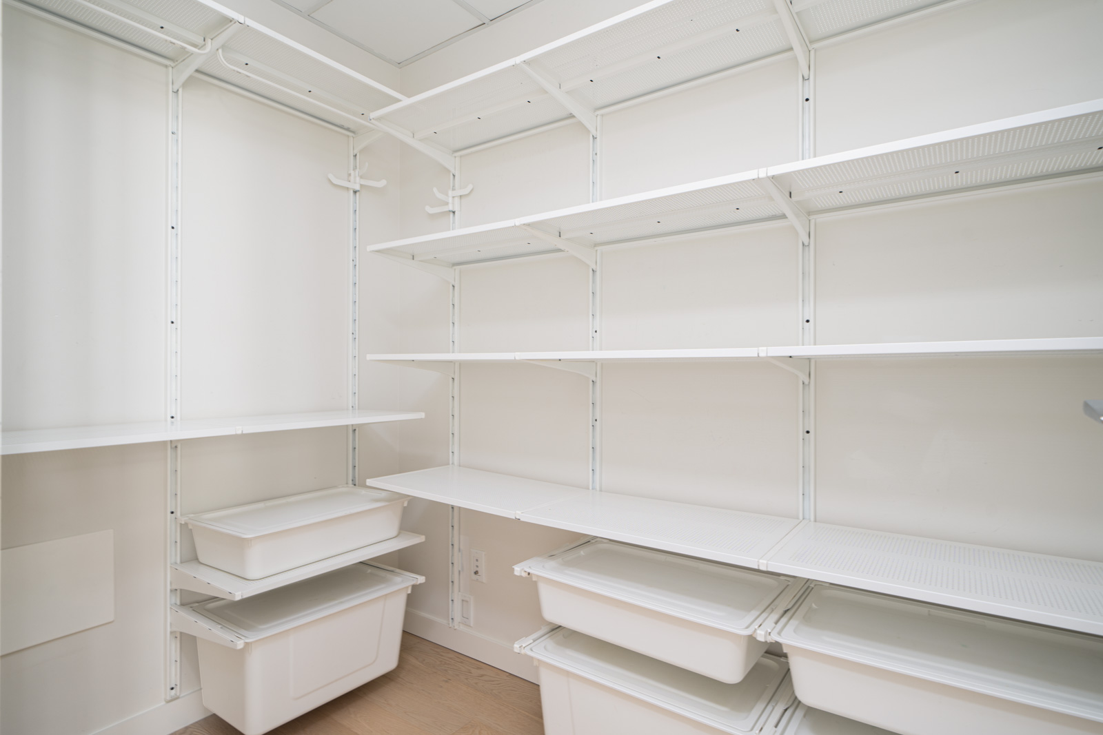 A white pantry with empty shelves and storage bins neatly organized along the walls.