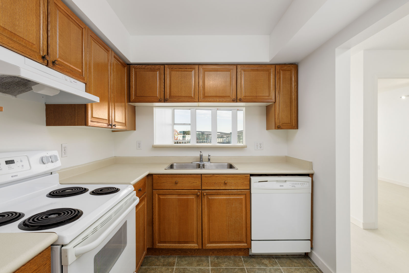 A kitchen featuring wooden cabinets, a white electric stove, a dishwasher, and a sink under a window with a view.