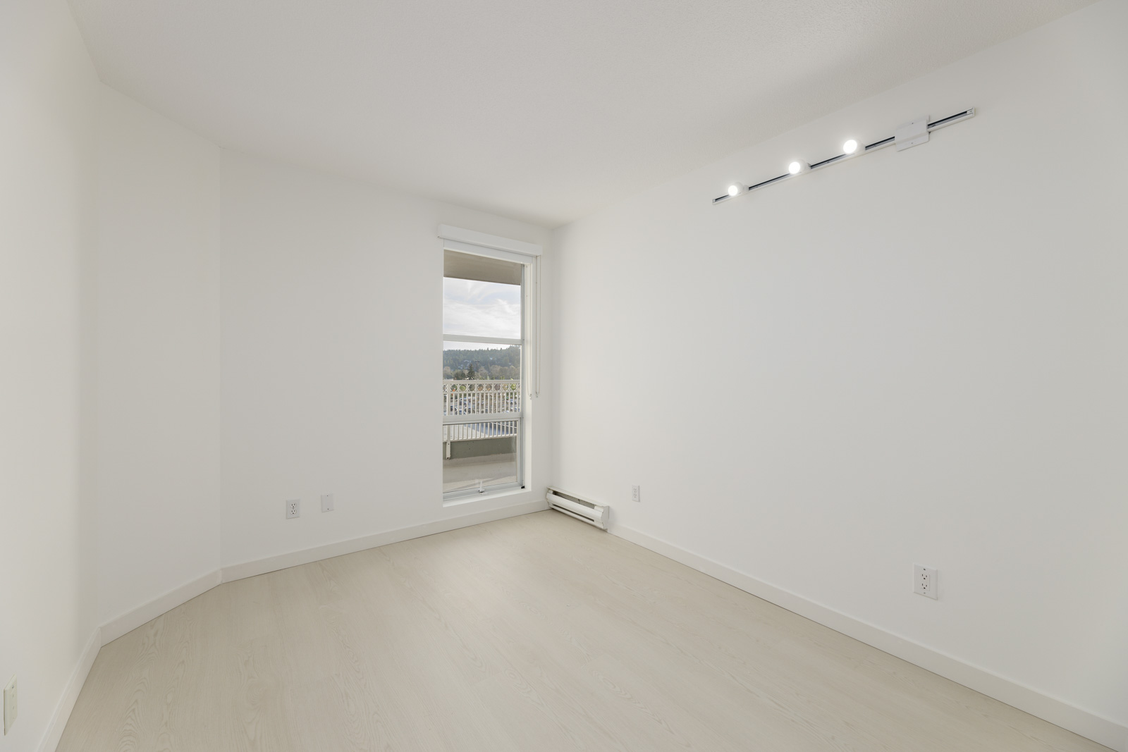 Empty room with light wood flooring, white walls, ceiling lighting, and a sliding door leading to a balcony with a view.