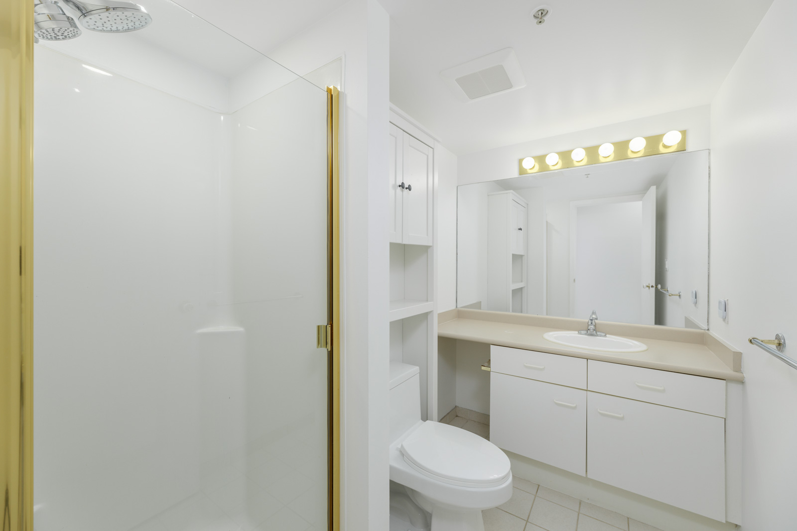 Bright white bathroom with a shower, sink, large mirror, and vanity lights.