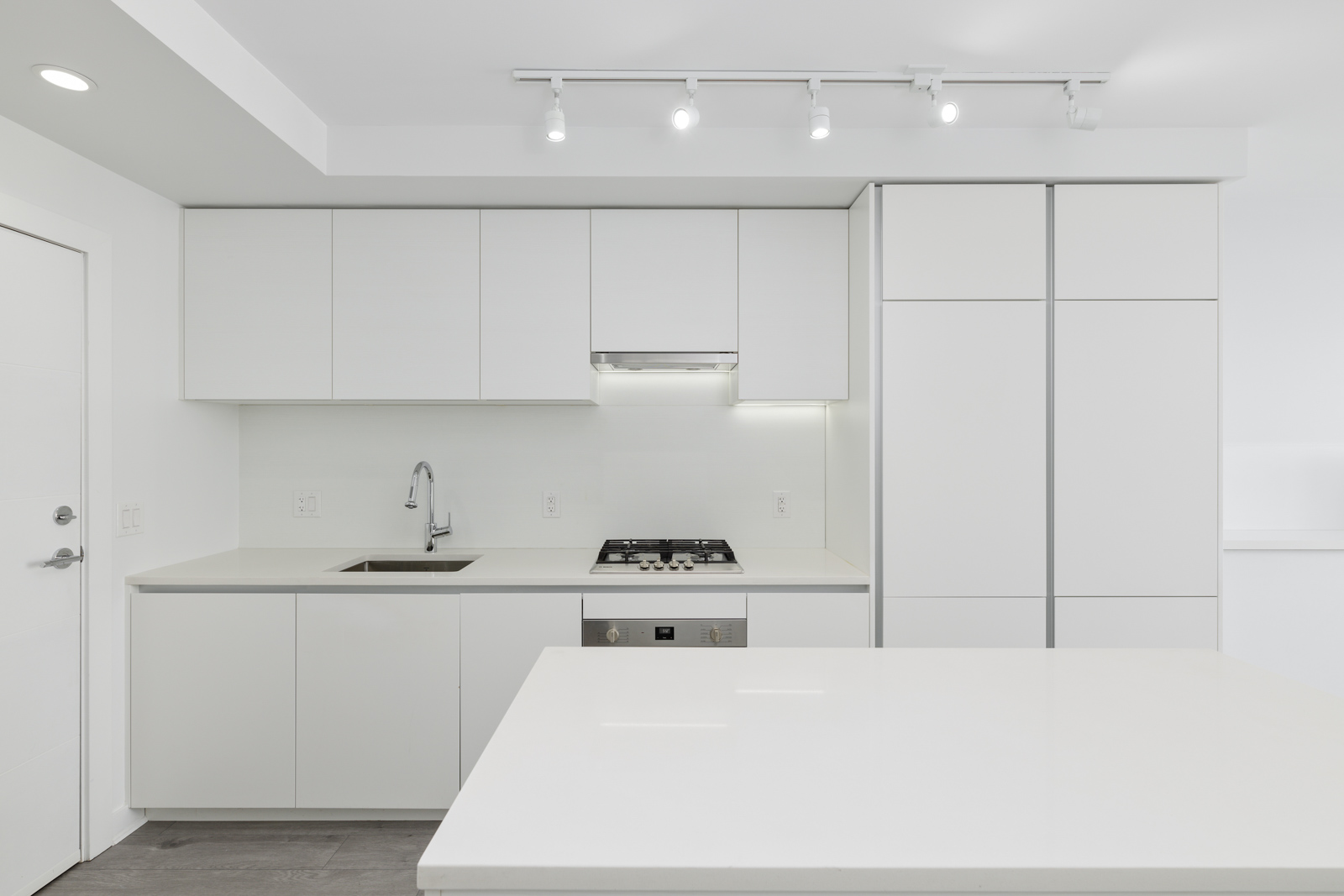Modern kitchen with white cabinets, stainless steel gas stove, and a large white countertop. Recessed lighting illuminates the space.