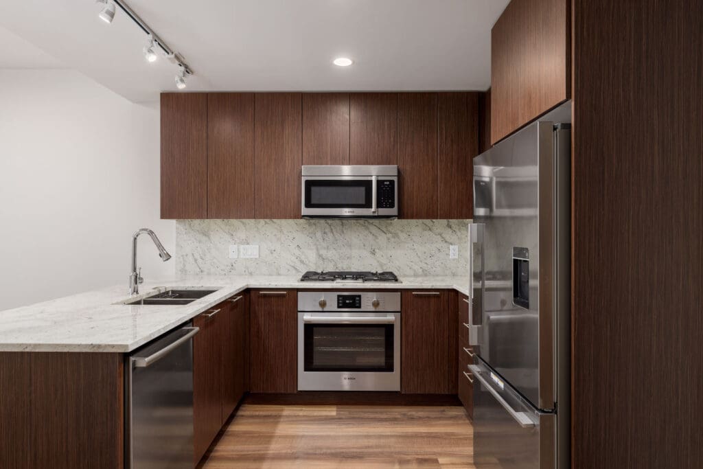 Modern kitchen with dark wood cabinets, stainless steel appliances including a refrigerator, oven, microwave, and dishwasher, and a marble countertop with a sink.