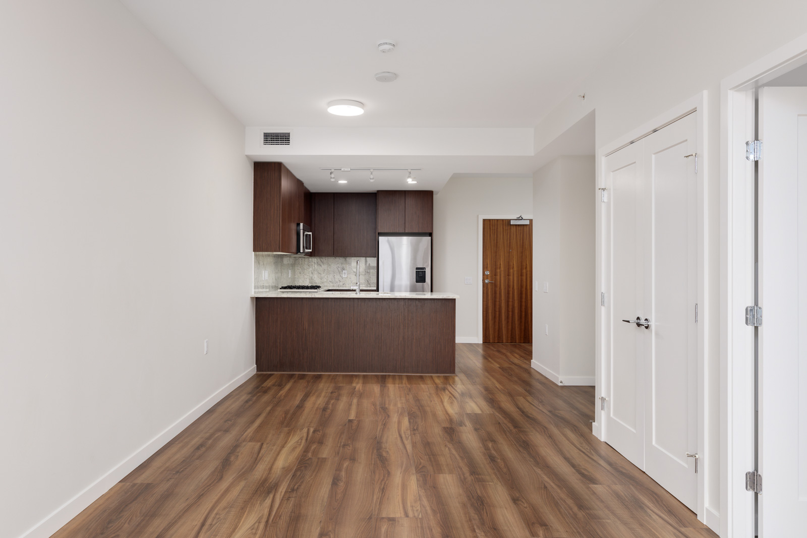 Modern kitchen and dining area with wooden flooring, dark wood cabinets, stainless steel appliances, and white walls.