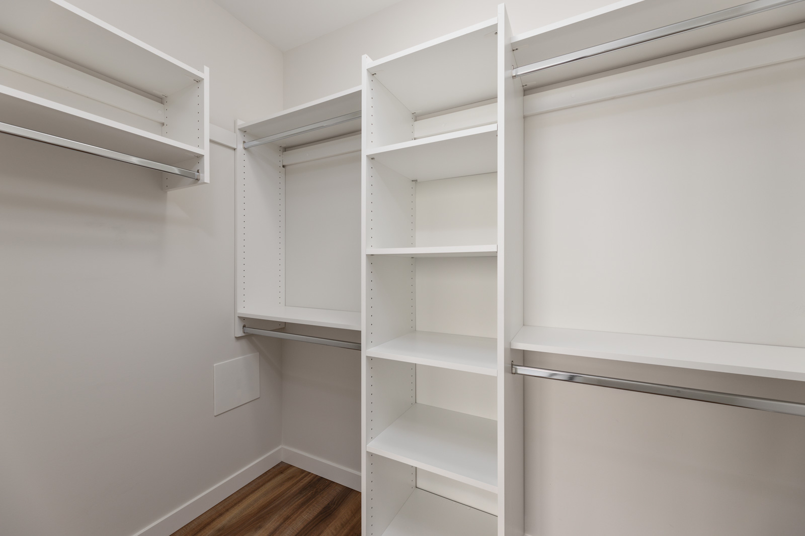 An empty walk-in closet with white shelving units and wooden floors.
