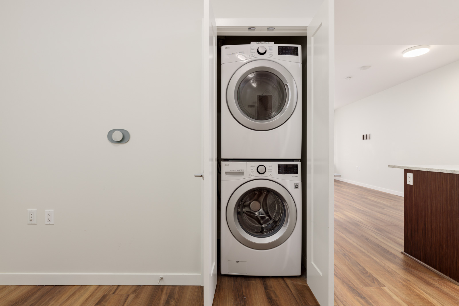 Stacked washer and dryer in a small utility closet with white doors, located in a room with wood flooring and white walls.