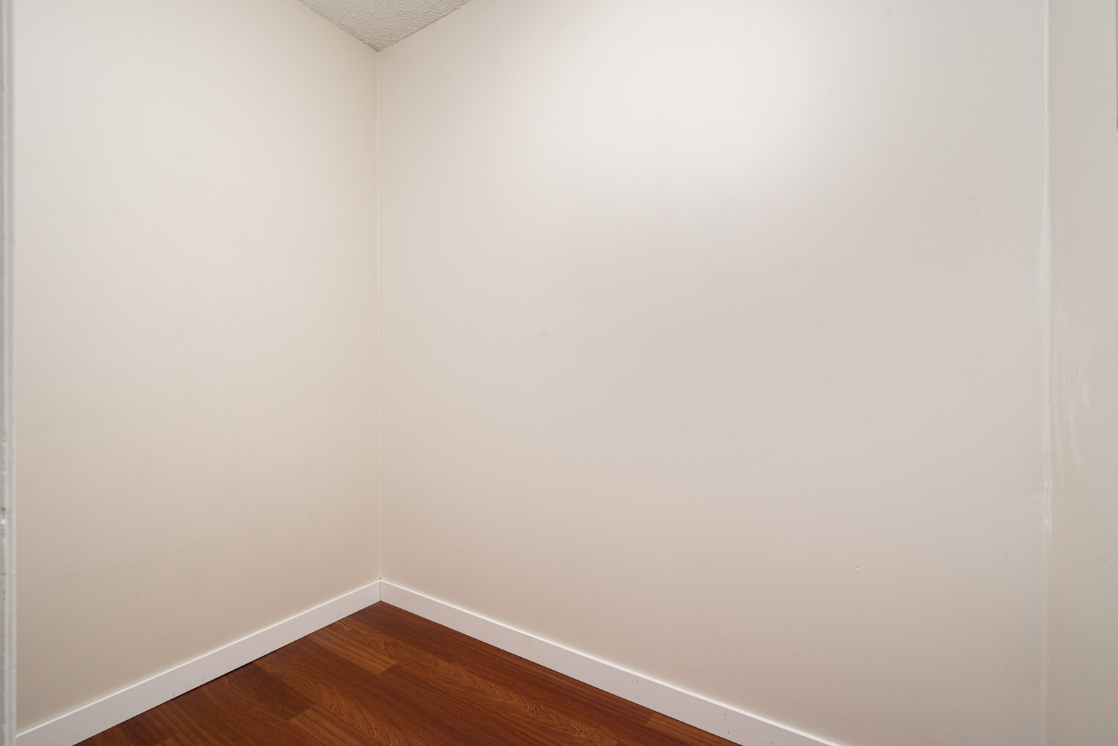 Empty room corner with white walls and wood flooring.