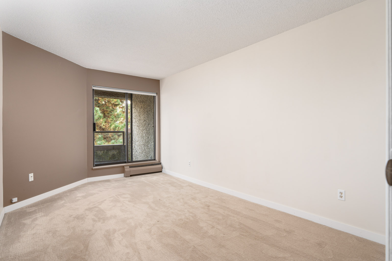 Empty room with beige carpet, white and brown walls, and a window with a patterned curtain.