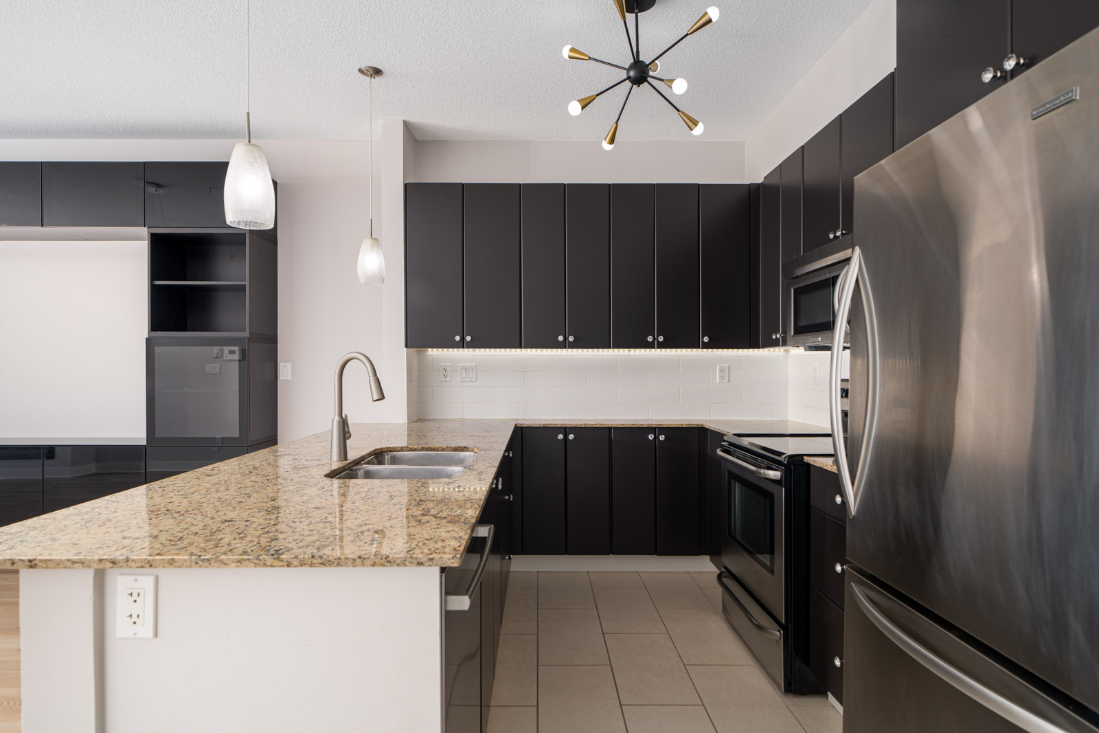 Modern kitchen with black cabinets, stainless steel appliances, granite countertops, and pendant lighting.