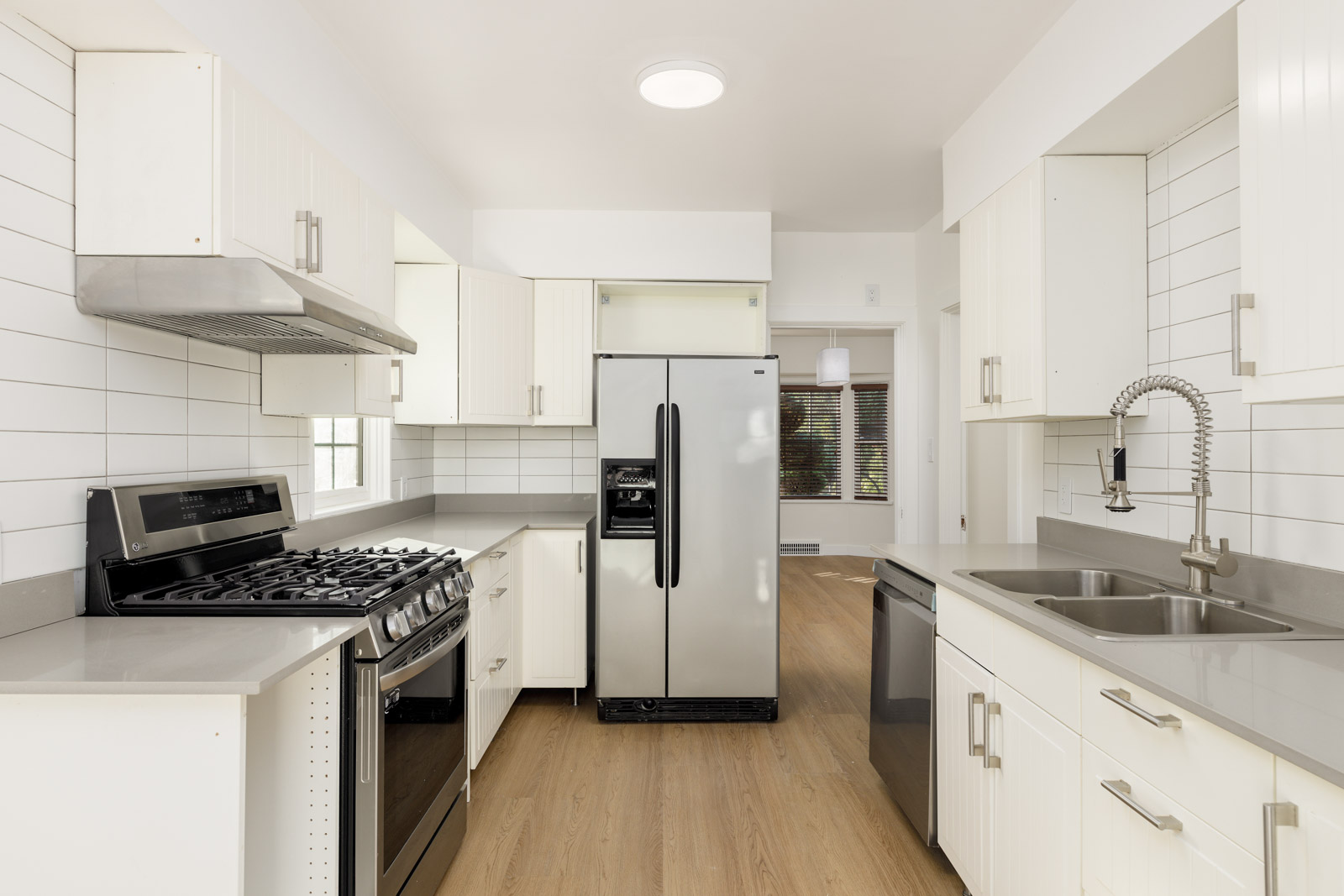 Modern kitchen with stainless steel appliances, including a refrigerator, stove, and dishwasher. White cabinetry and light wood flooring complement the space.