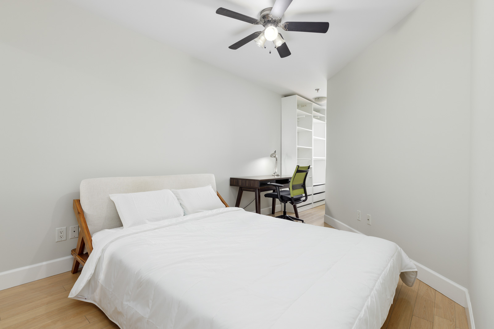Minimalist bedroom with a bed, white bedding, ceiling fan, and a desk with a green chair.