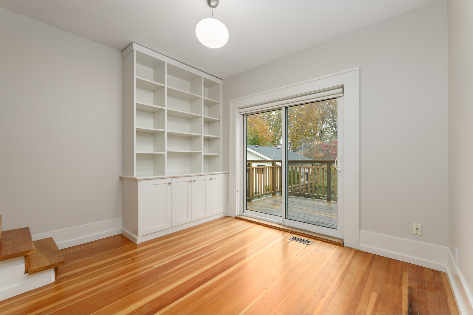 A room with hardwood floors, built-in white shelves, and a sliding glass door leading to a wooden deck outside.