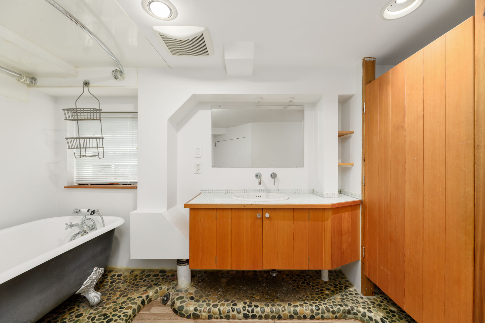 Bathroom with a freestanding bathtub, wooden vanity, large mirror, and stone-patterned floor.