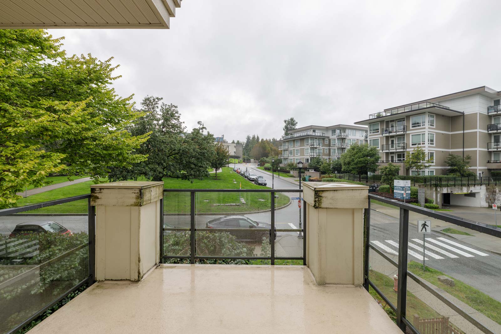 View from a balcony overlooking a street with parked cars, a crosswalk, and residential buildings on a cloudy day.