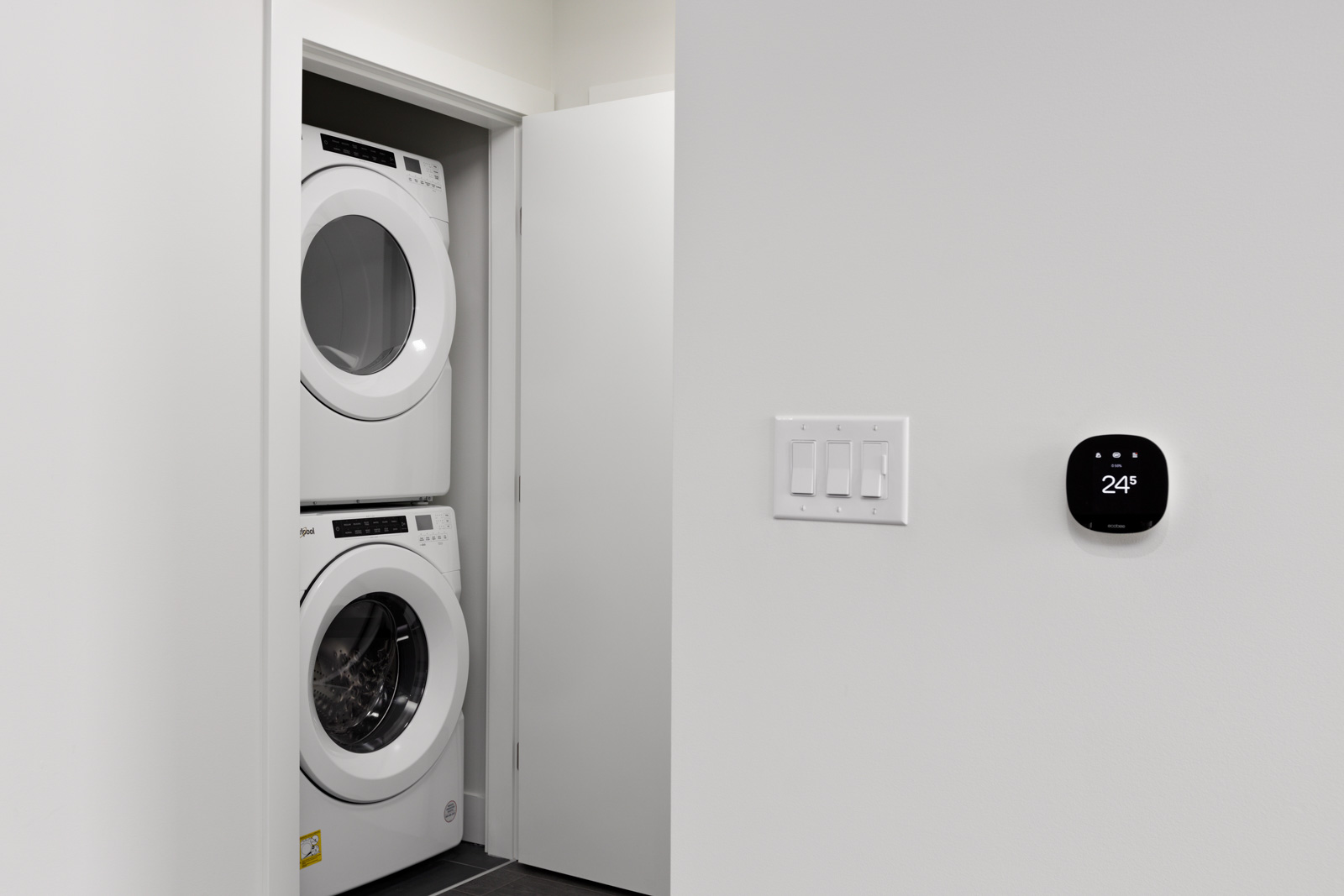 A stacked washer and dryer are visible through an open door. A digital thermostat on the wall displays 24 degrees.